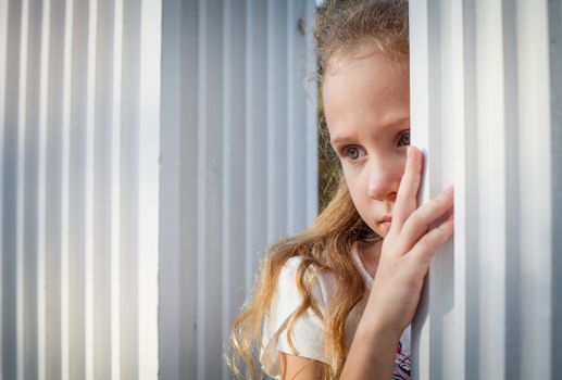 Sad little girl near the white wall.