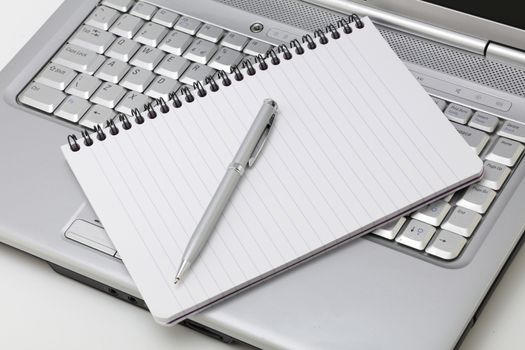 A notebook and pen resting on a laptop PC
