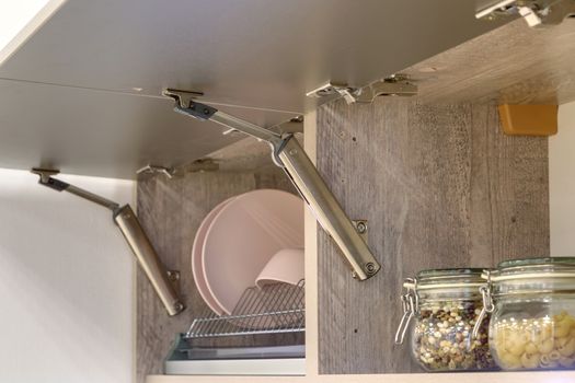 Fragment of the kitchen interior. Open hinged kitchen cabinet with utensils.