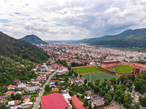 Aerial mountain city view with a small football stadium in front. Piatra Neamt aerial view in Romania