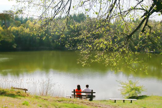 Two people on bench near the lake. Lake, mountain and sunlight