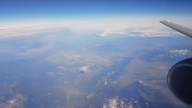 Sky and jet plane wing with  land below against the blue sky