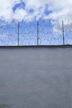 Barbed fence arround prison wall against sky