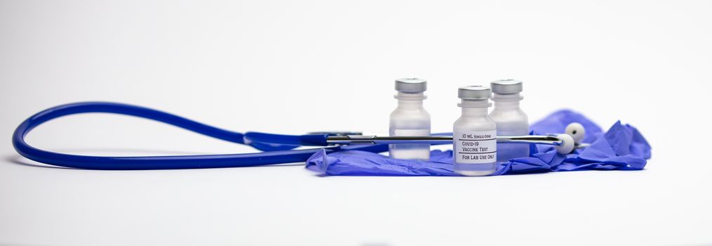Three Covid-19 test vaccine vials on top of blue medical gloves and surrounded by a blue stethoscope.