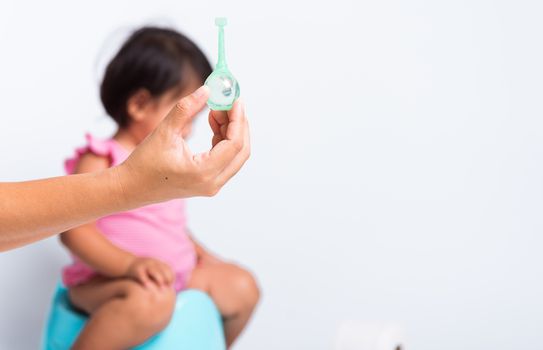 Asian little cute baby child girl training to sitting on blue chamber pot or potty her problem cannot shit and mother use Enema for help, studio shot isolated on white background, wc toilet concept