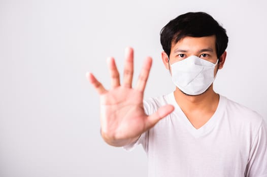 Closeup Asian handsome Man wearing surgical hygienic protective cloth face mask against coronavirus and raising hand stop sign, studio shot isolated white background, COVID-19 medical concept