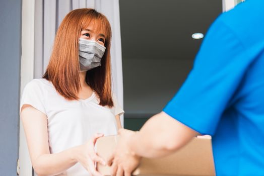 Asian young delivery man courier with package post box in uniform he protective face mask he making service woman customer receiving front house under curfew quarantine pandemic coronavirus COVID-19