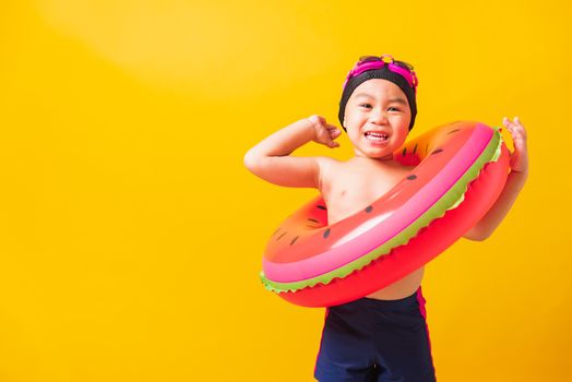 Summer vacation concept, Portrait Asian happy cute little child boy wear goggles and swimsuit hold watermelon inflatable ring, Kid having fun on summer vacation, studio shot isolated yellow background