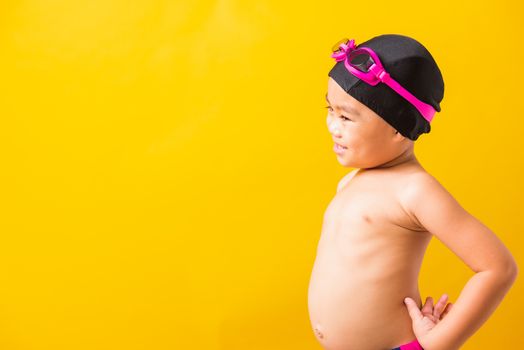 Summer vacation concept, Closeup portrait Asian happy cute little child boy wearing goggles and swimsuit, Kid having fun with in summer vacation looking side, studio shot isolated yellow background