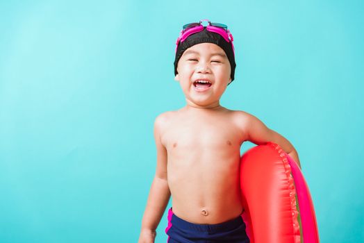 Summer vacation concept, Portrait Asian happy cute little child boy wear goggles and swimsuit hold watermelon inflatable ring, Kid having fun on summer vacation, studio shot isolated blue background