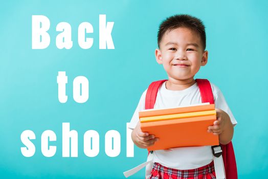 Back to school. Portrait Asian happy funny cute little child boy smiling and laugh holding books, studio shot isolated blue background. Kid from preschool kindergarten with school bag education