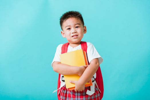 Back to school concept. Portrait Asian happy funny cute little child boy smiling and laugh hug books, studio shot isolated blue background. Kid from preschool kindergarten with school bag education