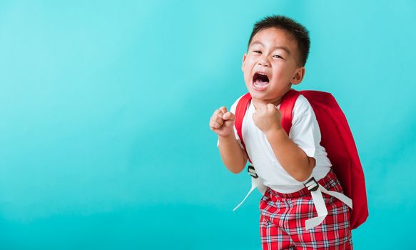 Back to school. Portrait happy Asian cute little child boy in uniform smile raise hands up glad when go back to school, isolated blue background. Kid from preschool kindergarten with school backpack