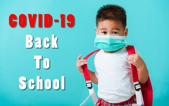 Back to school coronavirus Covid-19 education. Portrait Asian cute little child boy kindergarten wear face mask protective and school bag before going to school, studio shot isolated blue background