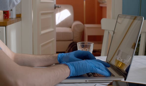 Close up male hands in protective rubber gloves typing on a keyboard. Man working from home. Remote work. Coronavirus epidemic