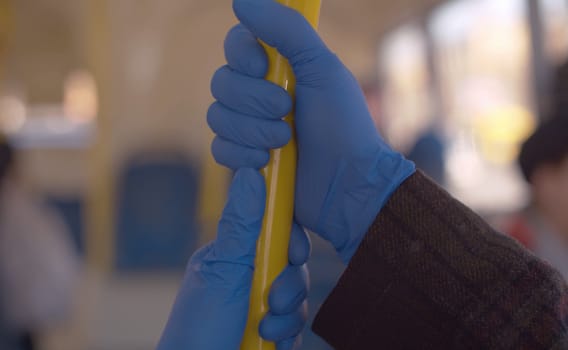Close-up of a two people wearing a blue latex gloves holding pole in a public bus. Coronavirus epidemic in the city. Healthy and safety lifestyle concept.