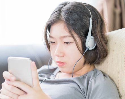 Close up young asian woman short hair listening music from mobile phone on the couch at home