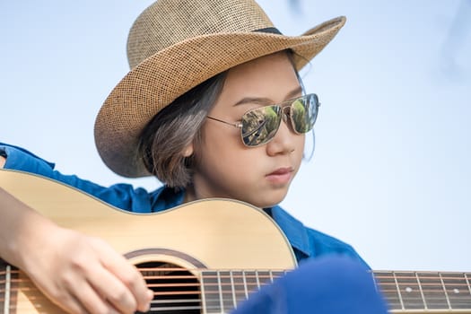 Close up young asian women short hair wear hat and sunglasses playing guitar in countryside Thailand