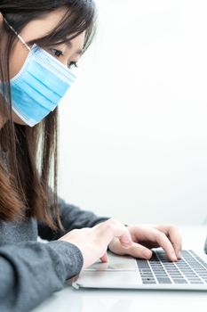 Woman using a laptop computer on the desk at home and wearing protective mask for protection against virus Covid-19