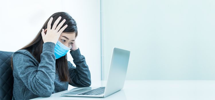 Woman using a laptop on the desk with headache and wearing  protective mask for protection against virus Covid-19