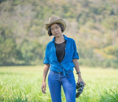 Young asian woman short hair wear hat and hold binocular in grass field countryside Thailand