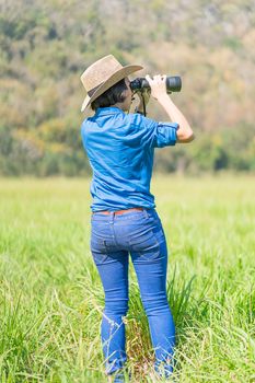 Young asian woman short hair wear hat and hold binocular in grass field countryside Thailand