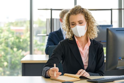 Young blonde staff in a suit with a face mask is taking notes of what to do after the meeting. Reduce the spread of Coronavirus disease 2019 (COVID-19) in the office.