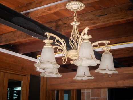 beautiful vintage interior background of a lighted retro chandelier hanging on a wooden ceiling, decorated lamp with flowers