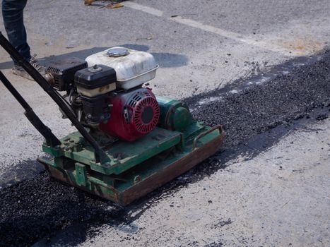 Worker use vibratory plate compactor compacting asphalt at road repair