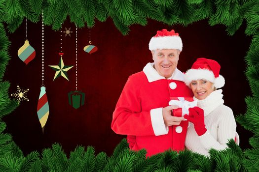 Festive mature couple holding gift against fir branches and christmas deocrations