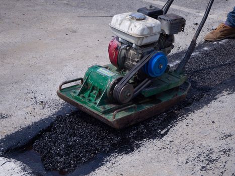 Worker use vibratory plate compactor compacting asphalt at road repair