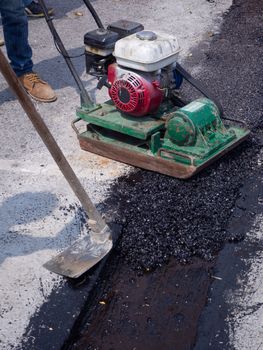 Worker use vibratory plate compactor compacting asphalt at road repair