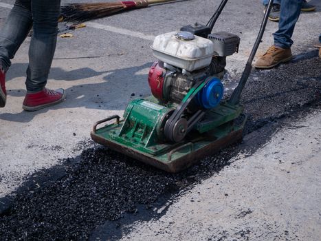 Worker use vibratory plate compactor compacting asphalt at road repair