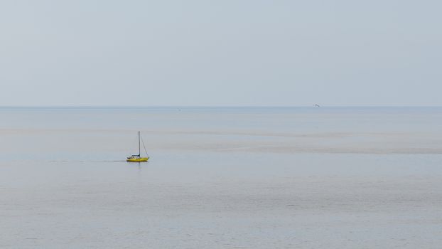 Yellow boat with its sails gathered up and stopped in a totally calm sea