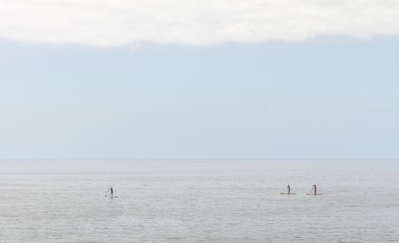 Three people practice paddle surfing in a totally calm sea