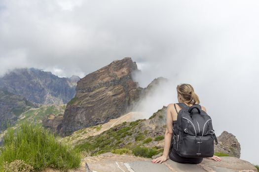 Girl with backpack sitting watching the fog on the mountains of Madeira Island, Portugal