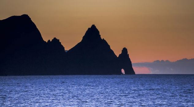 Sunset on the island of Madeira with the rocks of the coast and silhouette, the orange sky and the intense blue water