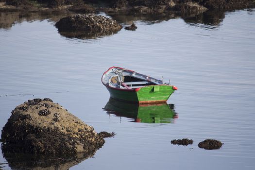 Green rowing boat moored on the seashore between rocks