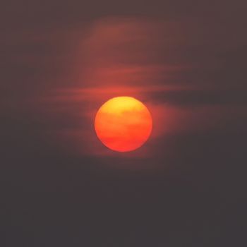 Close-up view of the sun at sunset in a dark sky with orange reflections