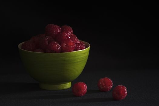 Raspberries in a green bamboo bowl on a black background