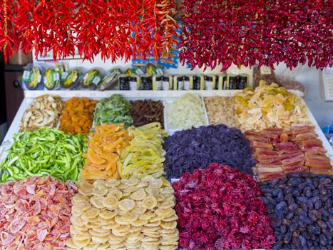 Chillies and paprika hanging over vegetables and dried fruit at a market stall.