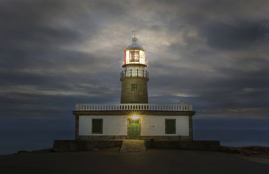 Corrubedo lighthouse, Spain illuminated at dusk with a cloudy sky in the background