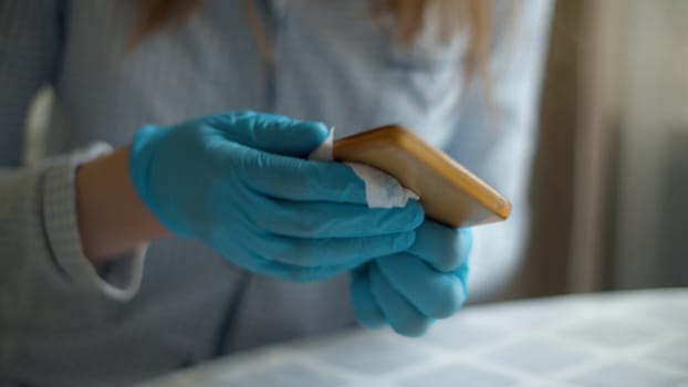 Close up hands in protective gloves cleaning smartphone with a disinfectant napkin. Hygiene during epidemic. Concept of safety life. Covid-19 pandemic