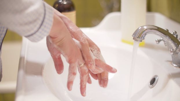 Woman scrupulously washing her hands. Close up female hands covered by soapy foam in a bright bathroom. Hygiene during epidemic. Covid-19 pandemic