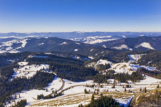 Evergreen forest and curvy road  in a winter landscape, aerial view
