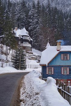 Winter scene in Red Lake Resort (Romania), snow covered houses and forest near road.