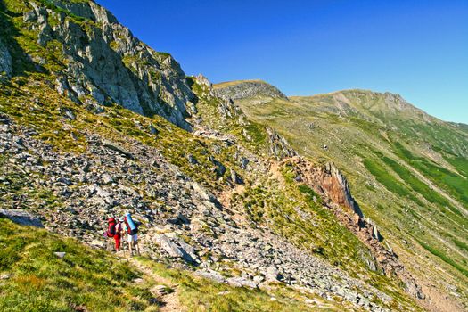 Summer mountain scene in Romanian Carpathians, two tourists hiking on mountain trail