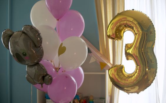 Birthday balloons in bright room. Balloons inflated with helium, sway slightly on a rope. Golden number 3 and brown bear. Close up