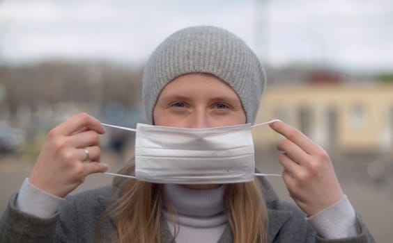 Close up portrait of a young handsome woman putting on a protective mask outdoors on the city background. Protect yourself and your loved ones. Covid-19 pandemic
