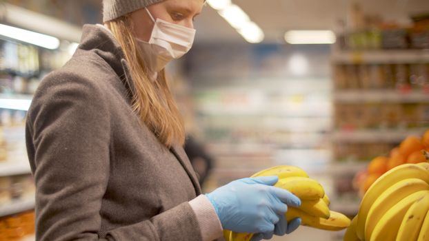 Portrait of the woman in protective mask and gloves choosing banana in the supermarket. Coronavirus epidemic in the city. Healthy and safety lifestyle concept. Covid-19 pandemic